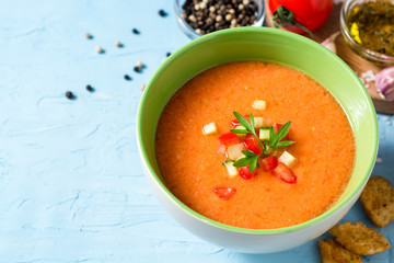 Summer cold soup gazpacho with parsley and vegetables on blue concrete background.