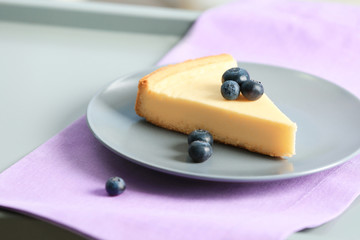 Plate with slice of delicious cheesecake and blueberry on violet napkin