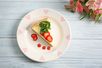 Plate with delicious cheesecake and sliced strawberry on wooden table