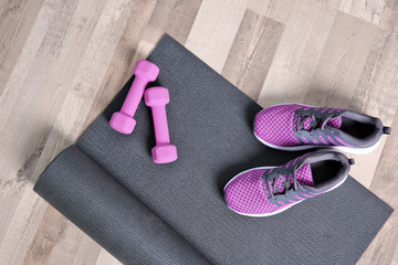 Yoga mat, sneakers and dumbbells on wooden floor