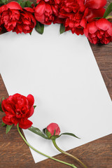 Composition of beautiful peonies and paper sheet on wooden background