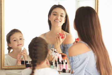 Young woman and her little daughter applying makeup at home