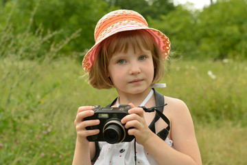 portrait of a baby photographer (a little girl) with a camera on the background of nature