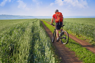 Fototapeta na wymiar Traveler with backpack Riding the Bike on the Beautiful Spring Mountain Trail