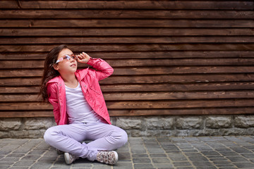 Stylish little girl child wearing a summer or autumn pink jacket, white jeans, sunglasses