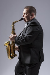 Fototapeta na wymiar Music Concepts. Portrait of Caucasian Mature Concentrated Saxophone Player Playing the Instrument Against White Background.