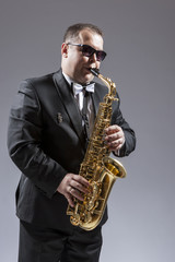 Obraz premium Music and Musicians Ideas and Concepts. Portrait of Caucasian Mature Saxophone Player in Sunglasses Playing the Instrument Against White.