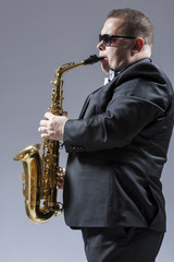 Fototapeta na wymiar Music Ideas and Concepts. Portrait of Mature Caucasian Saxophone Player in Sunglasses Playing the Saxophone in Studio Environment.