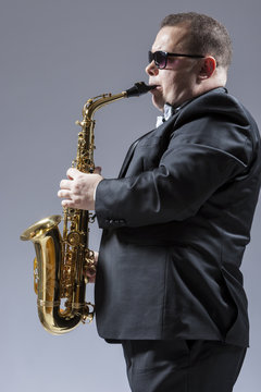 Music Ideas and Concepts. Portrait of Mature Caucasian  Saxophone Player in Sunglasses Playing the Saxophone in Studio Environment.