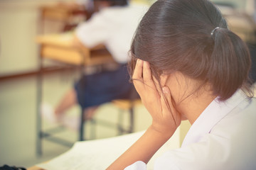Girl thoughtful student sitting in rows exams studying at table with her head tilted back as her tries to solve a problem or seek inspiration in seat rows at exam class room at high school, 