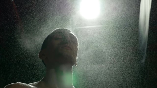 Slow motion of kickboxer cooling under cold water vapors in gym studio after training