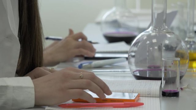 Students at work in the laboratory of chemistry take notes in a notebook. Female Pupil Using phone In Science Lesson. Young medical students write