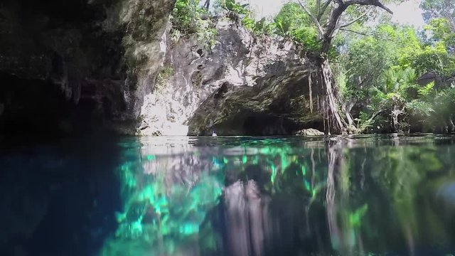 SLOW MOTION UNDERWATER Woman snorkeling in crystal clear river exploring stunning beauty of an ancient Grand Cenote sinkhole under a jungle-framed sky. Lush foliage hanging from the edge of rocky wall