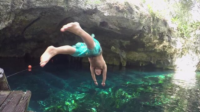 Slow motion closeup young men on vacation in sunny Mexico diving into crystal clear cenote water