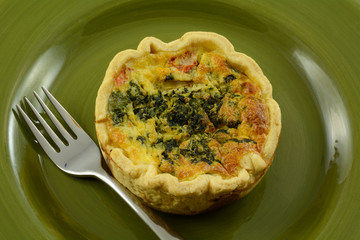 Individual portion quiche florentine with spinach, feta cheese and tomato in green plate