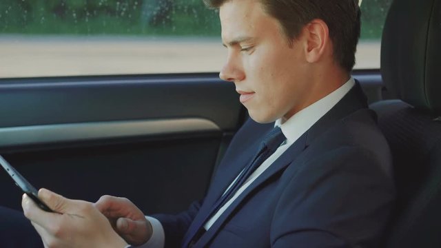 Thoughtful handsome businessman using tablet in the car 4K