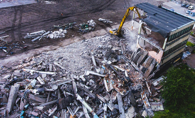 A process of buliding demolition, demolition site with heavy bulldozer and excavator with crushing equipment at work, demolished house, shot from air with drone
