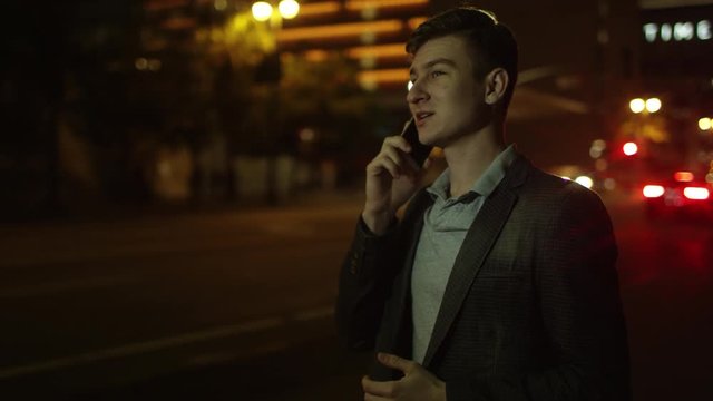 Young handsome man is having a phone talk and trying to catch a taxi