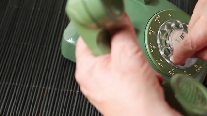 A senior man holds the handset while dialing an old rotary phone with room for text