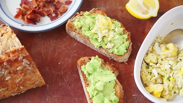 Adding herb scrambled eggs and bacon pieces to avocado toast on artisan bread