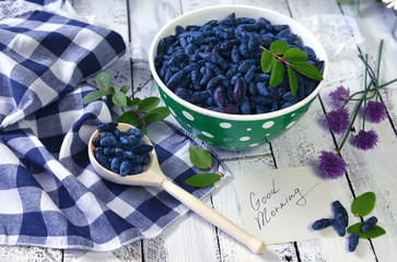 Note with good morning text, spoon and bowl full of ripe berries. Beautiful summer rural background