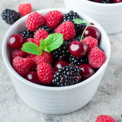 Close up of Summer fresh berries in white bowl on gray concrete table background. Vegetarian food - raspberry, blackberry and cherry