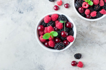 Summer fresh berries in white bowl on gray concrete table background. Top view with copy space. Vegetarian food - raspberry, blackberry and cherry