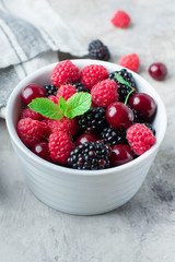Close up of Summer fresh berries in white bowl on gray concrete table background. Top view with copy space. Vegetarian food - raspberry, blackberry and cherry