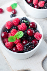 Close up of Summer fresh berries in white bowl on gray concrete table background. Vegetarian food - raspberry, blackberry and cherry