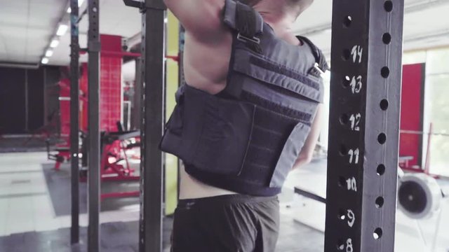 Athlete with a weighted vest doing pull ups in the Gym. Slow motion