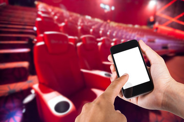Smartphone on hand and white screen with blurry background of seat in movie theater.