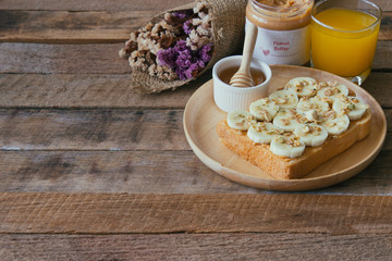 Banana peanut butter toast sandwich on wood plate with honey. Homemade open sandwich spread with peanut butter on top with banana slice and granola. Delicious healthy sandwich for breakfast or lunch.