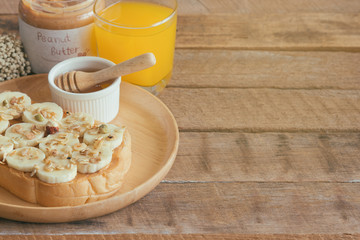Banana peanut butter toast sandwich on wood plate with honey. Homemade open sandwich spread with peanut butter on top with banana slice and granola. Delicious healthy sandwich for breakfast or lunch.