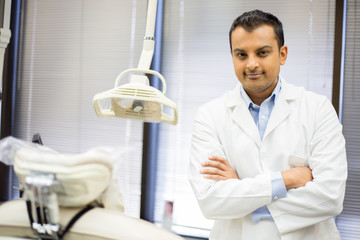 Closeup portrait of confident healthcare professional with arms folded standing next to white patient chair