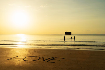 "Love" written on golden sandy beach. Silhouette