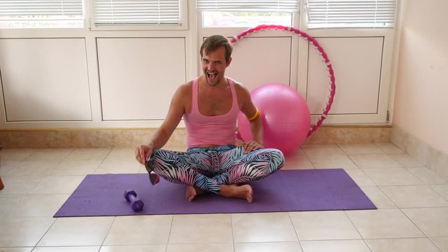 A playful handsome guy in a pink T-shirt and blue leggings is engaged in fitness depicting a girl. Slow motion