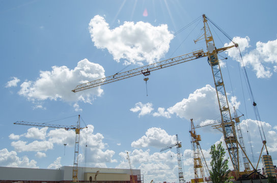 Construction cranes against a blue cloudy sky