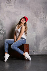 Smiling young woman sitting on suitcase, before travel, indoor, positive