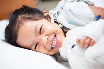 Sick asian child girl is lay down on the bed and smiling when she feel better in the hospital