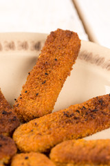 Fried fish meat sticks on the plate above wooden planks  table