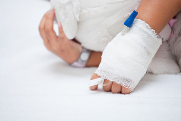 Sick child girl's hand with saline intravenous (iv) drip hugging her doll while sleeping in the hospital