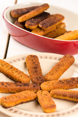 Fried fish meat sticks on the plate above wooden planks  table