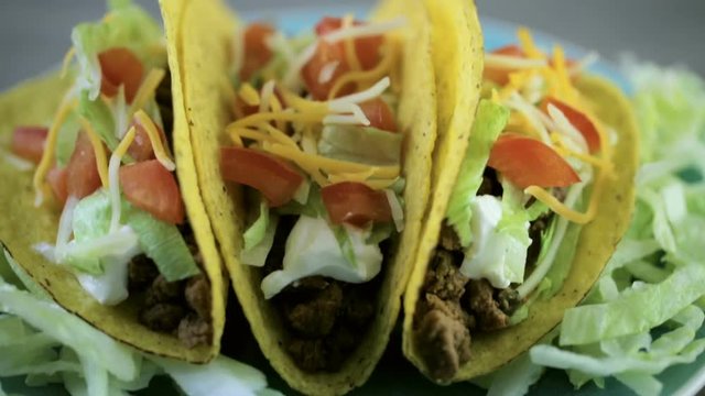 Close up of fresh beef tacos in hard yellow corn taco shell with sour cream and shredded cheese