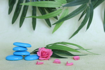 Des galets décoratif empilés à la façon zen avec une fleur rose sur fond vert et feuillage