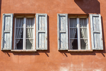 Orange wall with two windows with blue shutters and white curtains in Bologna, in Italy