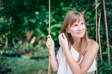 Portrait of the beautiful long hair women  in white dress sitting on the swing in the tropical garden