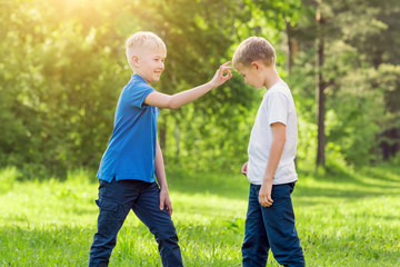 Fototapeta premium Blond boy click his finger on the forehead of his friend in a sunny park