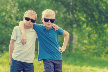 Two blond boy in sunglasses standing embracing  in the park