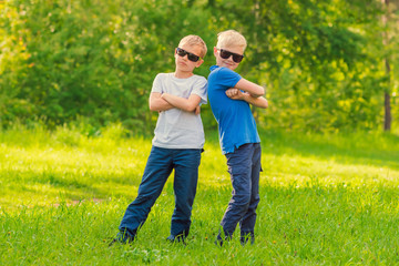 Fototapeta premium Two blond boy in sunglasses standing next to each other outdoors in the park