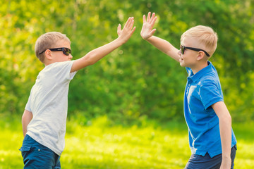 Two blond boys in sunglasses give five their hands in the summer park
